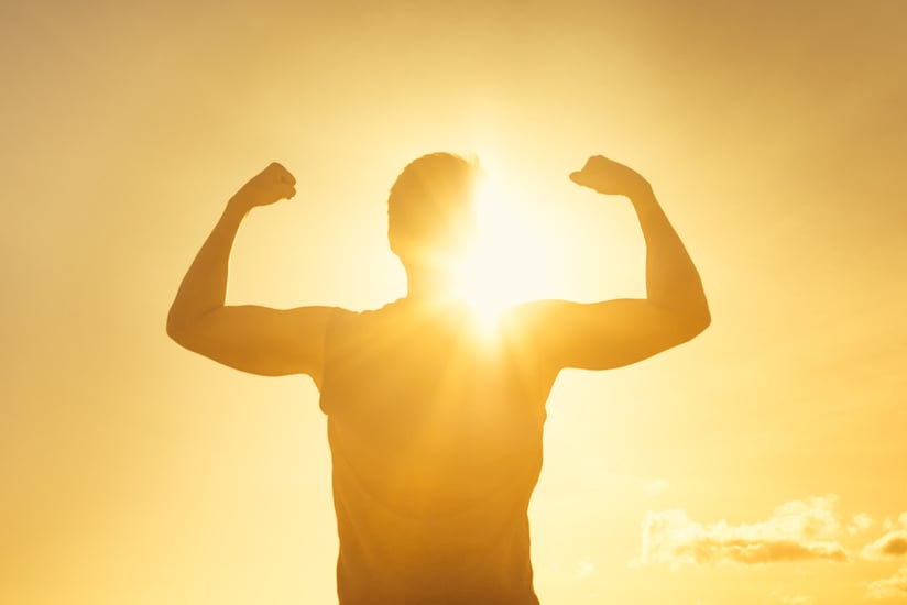 Strong confidant man flexing on sunset background.